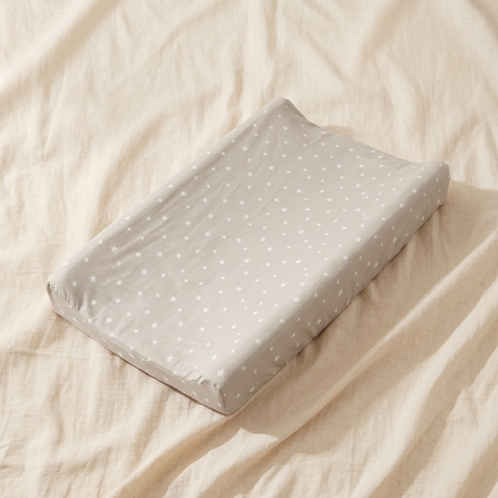Baby changing pad with soft grey dotted cover on cream linen background