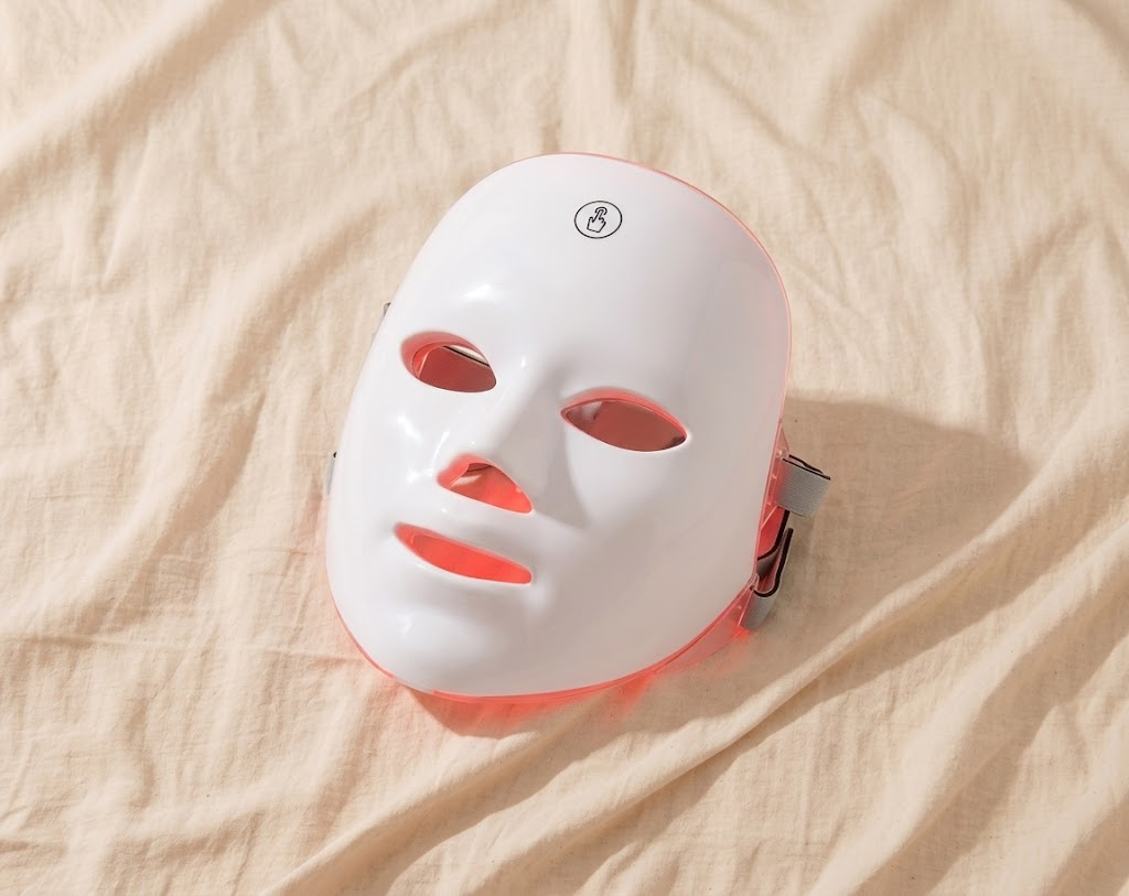 7-colour LED photon facial mask glowing red on cream linen background
