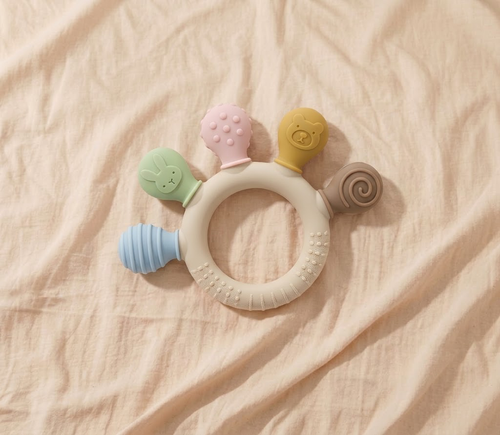 Baby sensory silicone ring teether with pastel coloured animal and textured attachments on cream linen
