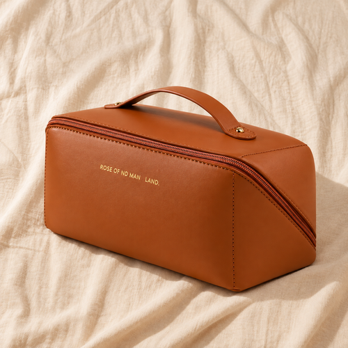 Tan brown leather cosmetic bag with gold zipper and handle on cream linen