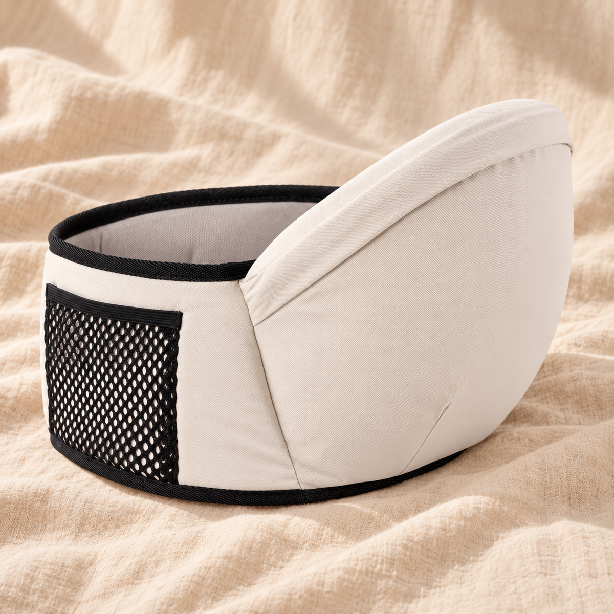 Cream baby hip-seat waist belt with black trim and mesh side pocket on warm beige linen