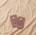 Pair of dusty rose baby knee pads with grip dots and bunny and bear details on warm beige linen