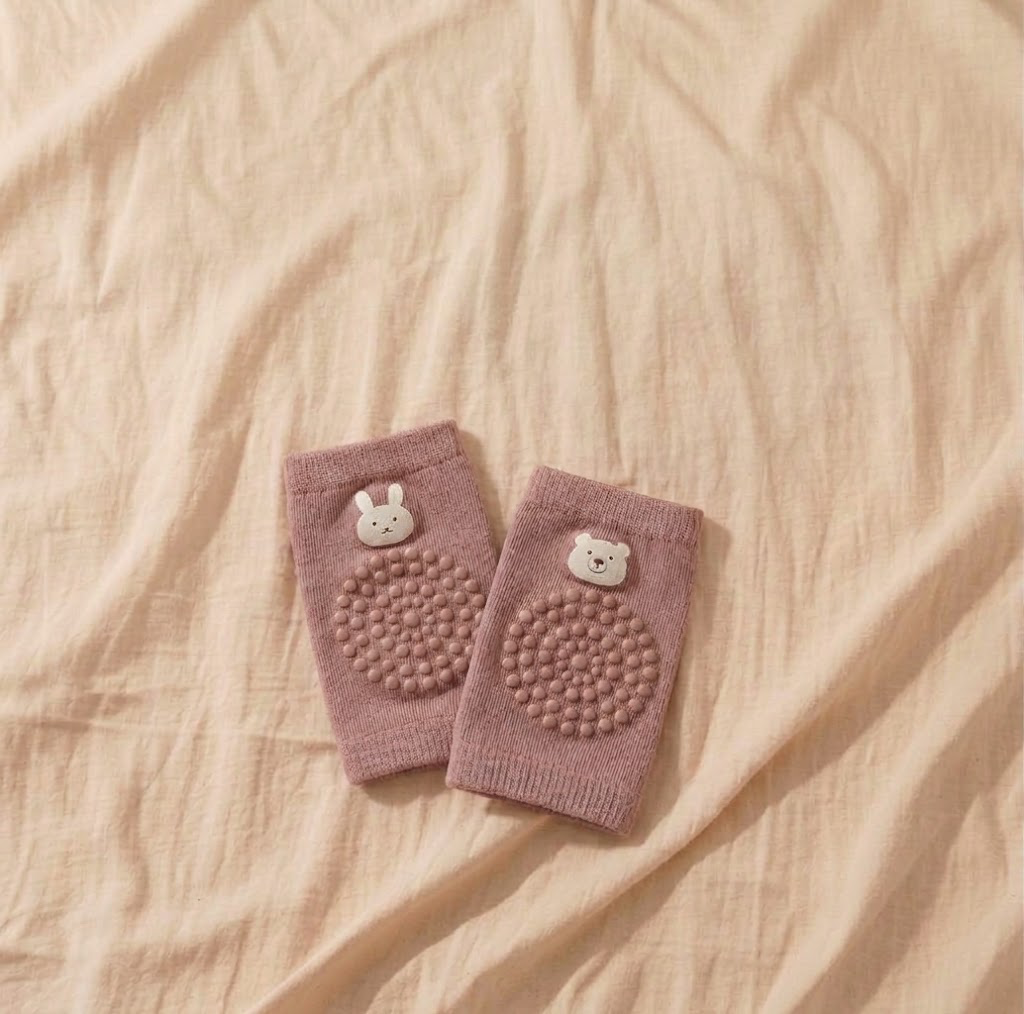 Pair of dusty rose baby knee pads with grip dots and bunny and bear details on warm beige linen